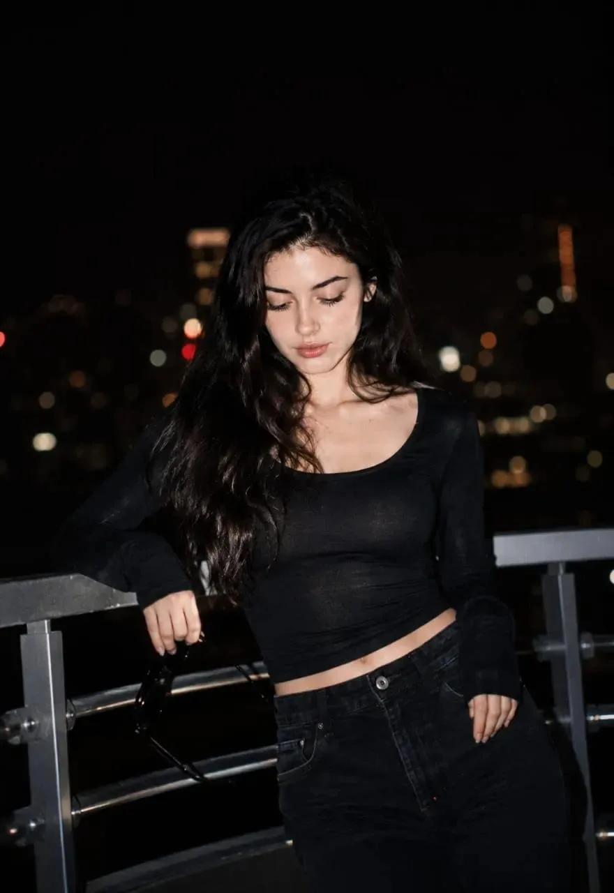 Cinematic Ultra-realistic night portrait of a young woman wearing dark top with dark jeans.