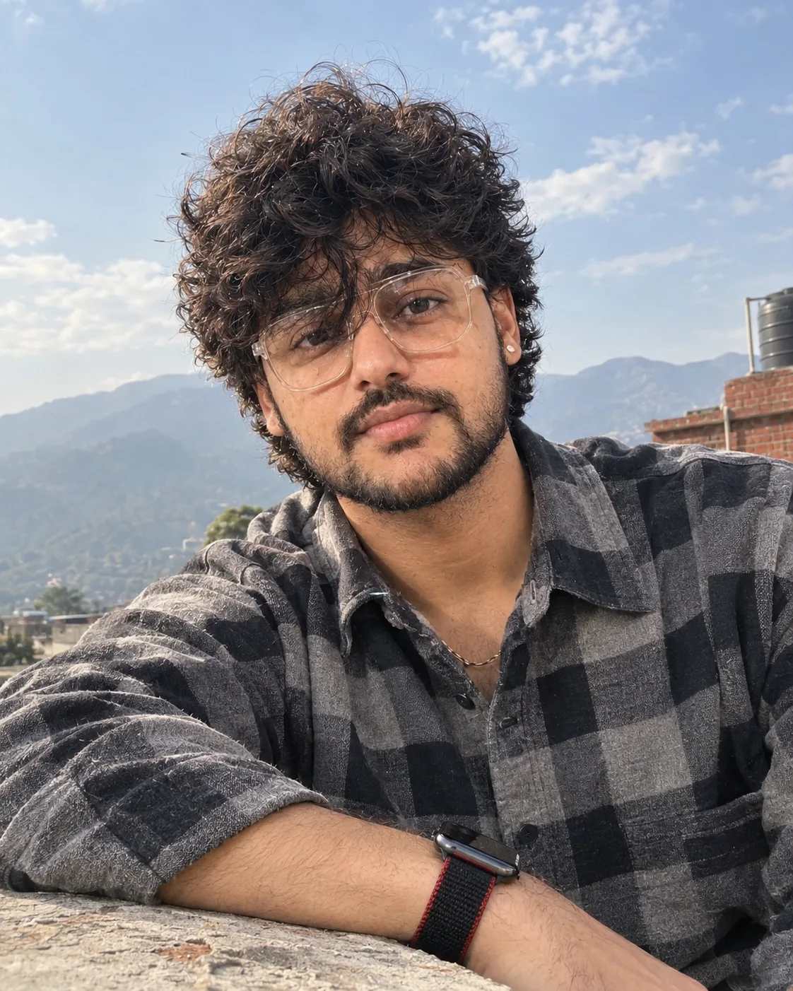 "A close-up selfie-style portrait of a young man with thick, voluminous black curly hair styled in a messy fringe that falls over his