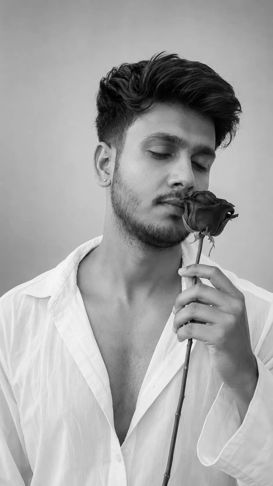 Create a cinematic black-and-white portrait of a young man with voluminous textured hair and a neatly trimmed beard, wearing a loose white