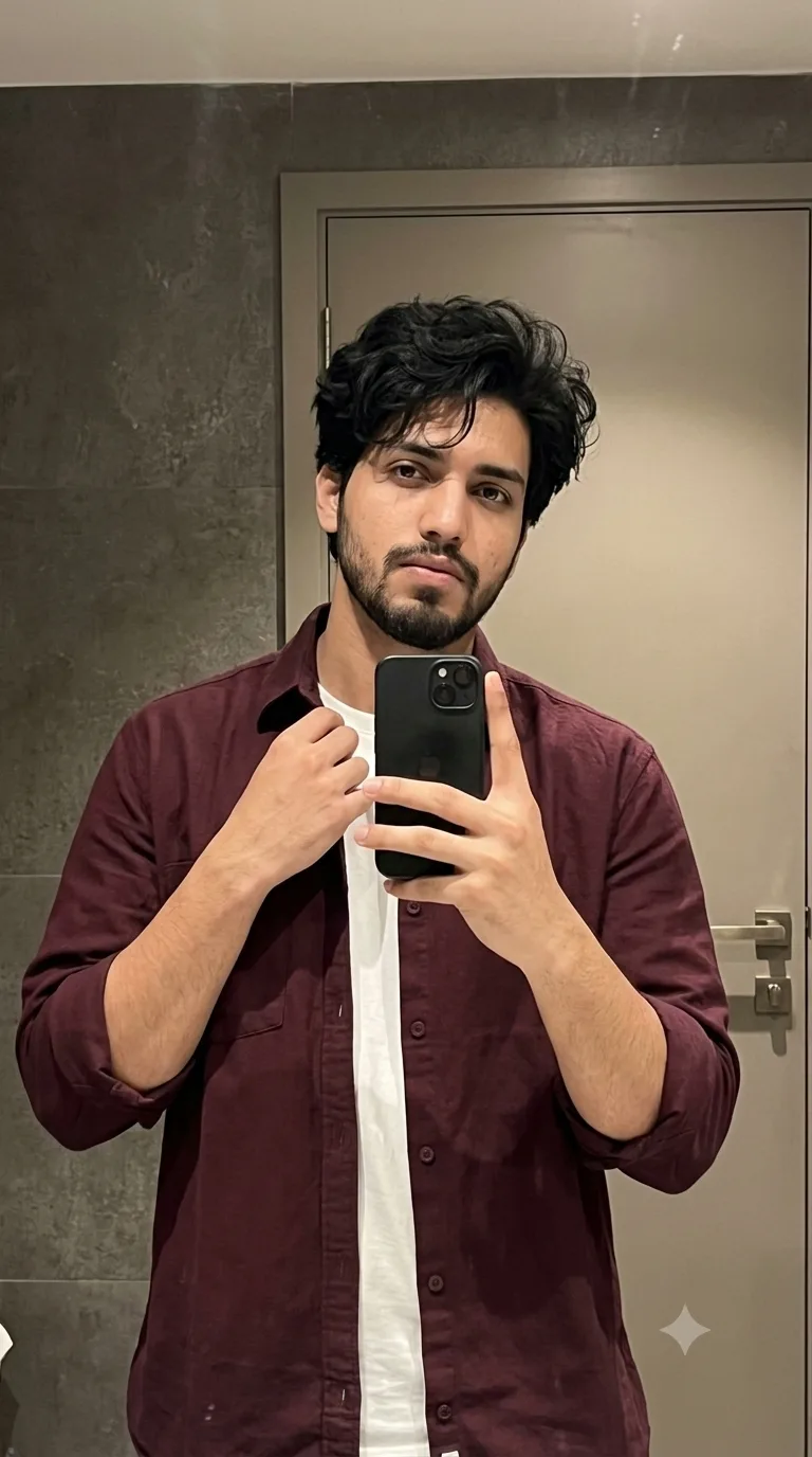 Ultra-realistic mirror selfie of a young man with thick, naturally wavy messy black hair, soft textured hairstyle falling slightly over the