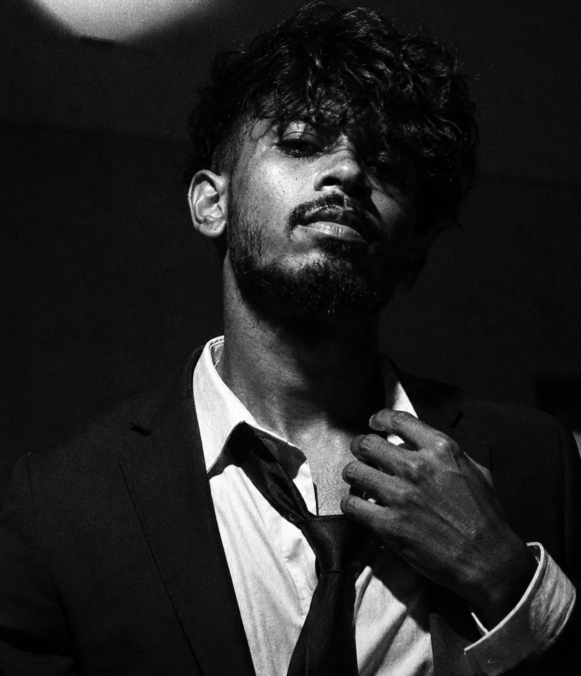 Create an ultra-realistic cinematic black-and-white editorial portrait of a young man in a sophisticated black suit, crisp white dress
