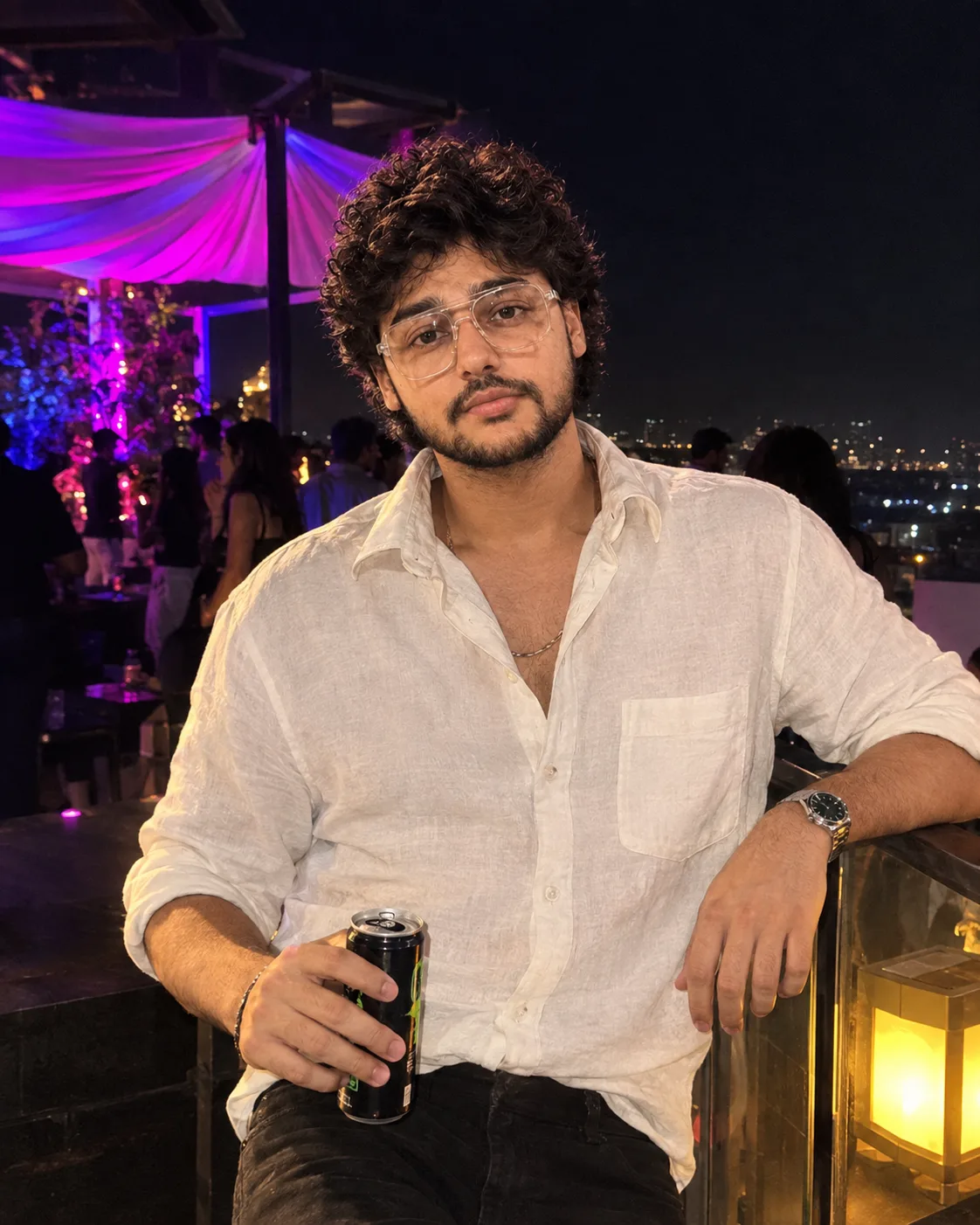 "A candid nightlife portrait of a young man with short, tousled black wavy hair falling over his forehead, looking at the camera with a