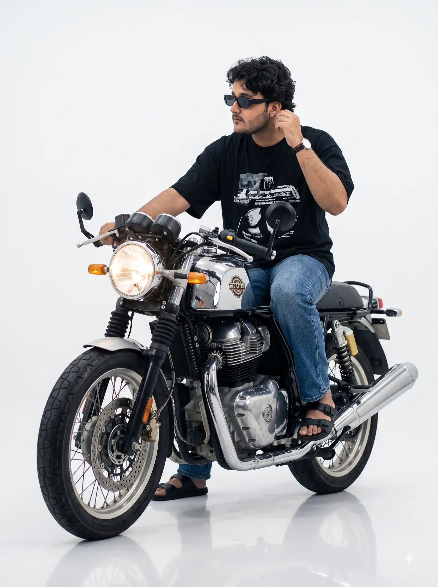 A stylish young man with curly hair sitting on a classic retro café racer motorcycle, looking to the side while adjusting his ear, wearing