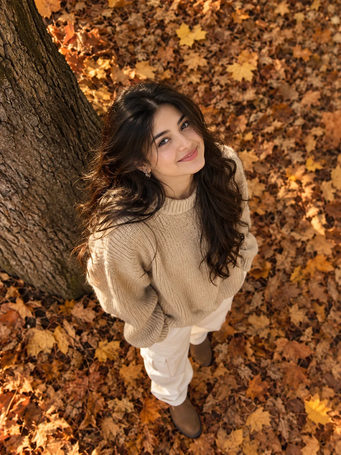 > ULTRA-REALISTIC CINEMATIC TOP-DOWN PHOTOGRAPH OF A YOUNG SOUTH ASIAN WOMAN STANDING BESIDE A LARGE TREE TRUNK, LOOKING DIRECTLY UP AT THE