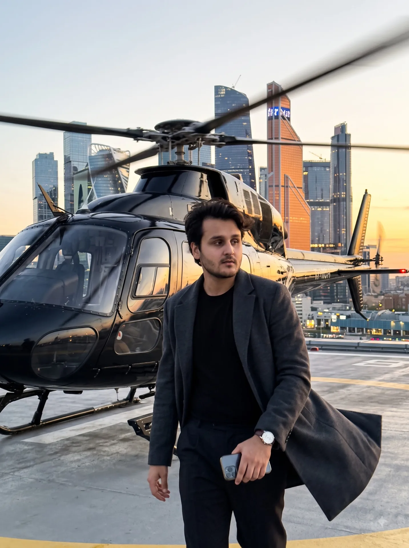 Photo 9:16 on iPhone. Face strictly according to reference. The man is walking away from a black helicopter. Helipad, helicopter platform