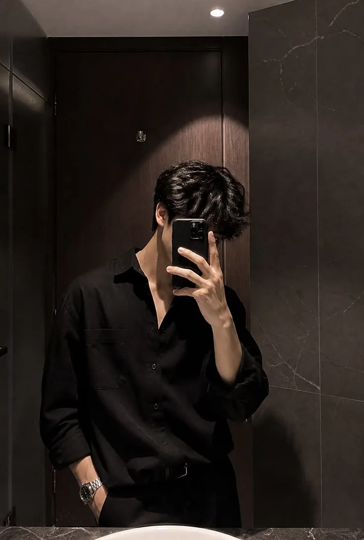 Create a highly realistic, cinematic mirror selfie of a young male model in a luxurious, dark modern bathroom.