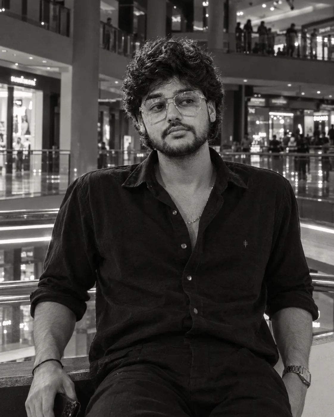 "A moody black-and-white portrait of a young man with thick, soft, tousled dark curly hair falling over his forehead, gazing off to the