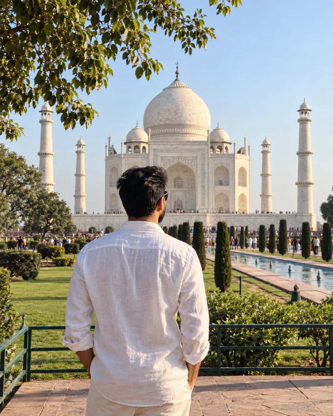 Create a photorealistic vertical travel photograph of a young adult man standing in the gardens of the Taj Mahal in Agra, India,