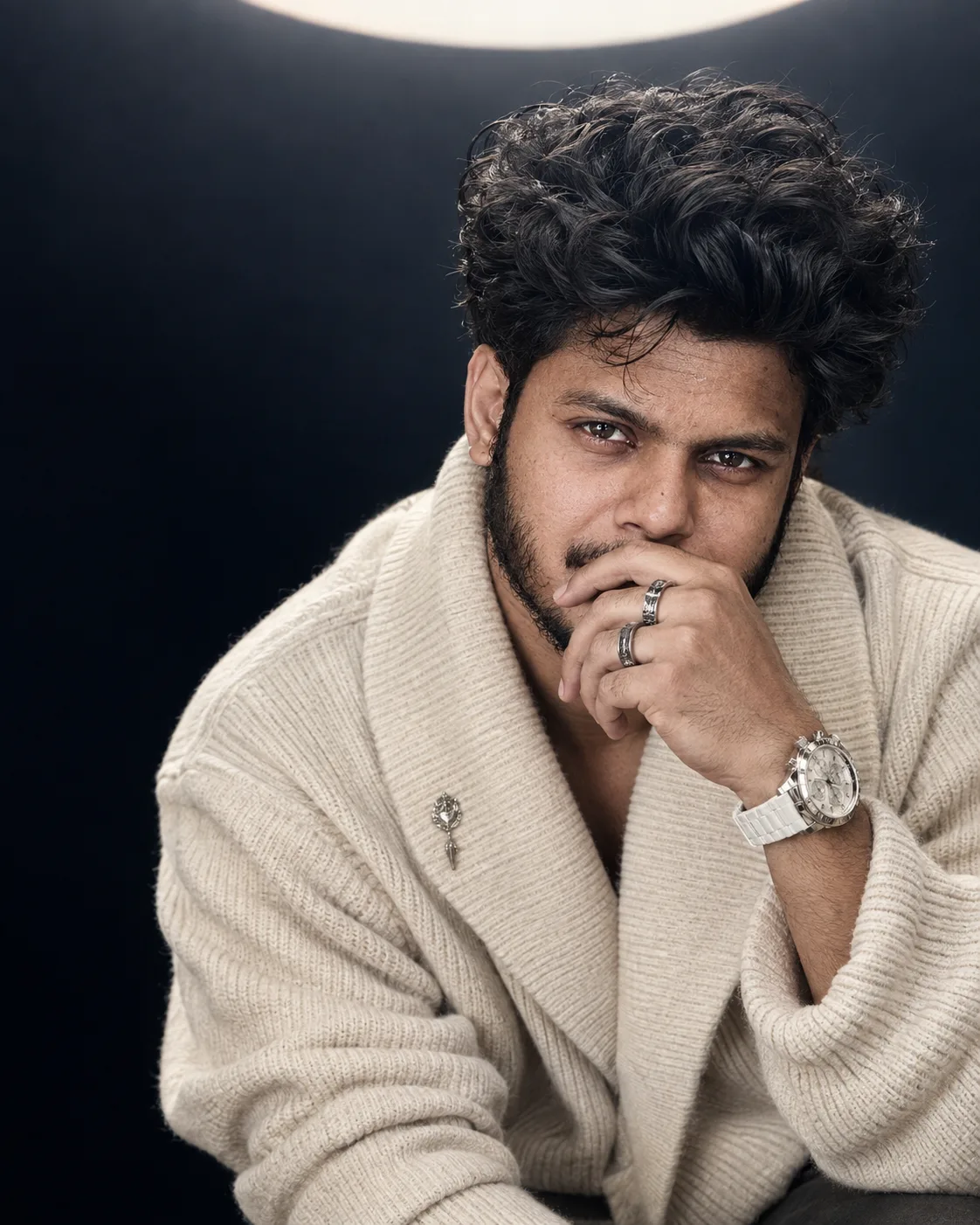 A close-up cinematic portrait of a young South Asian man with voluminous, messy dark curly hair and a short beard, intense dark eyes