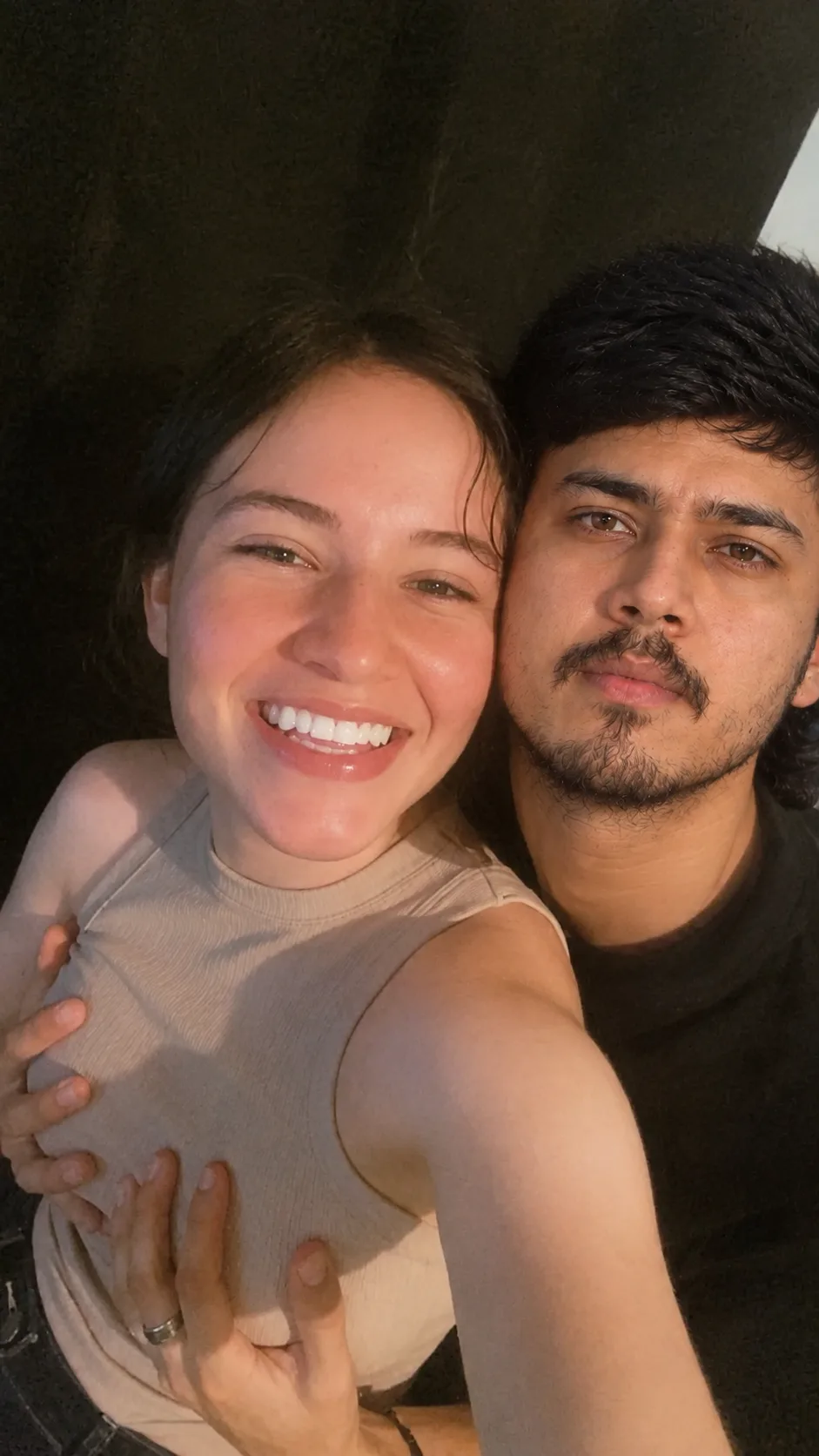 “Create a realistic, candid close-up smartphone selfie of a young couple sitting closely together at night.