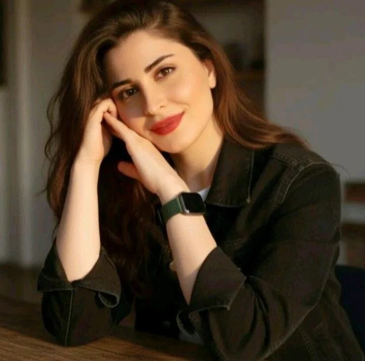 A high-quality, realistic cinematic portrait of a beautiful young Pakistani woman sitting at a wooden table, resting her cheek gently on