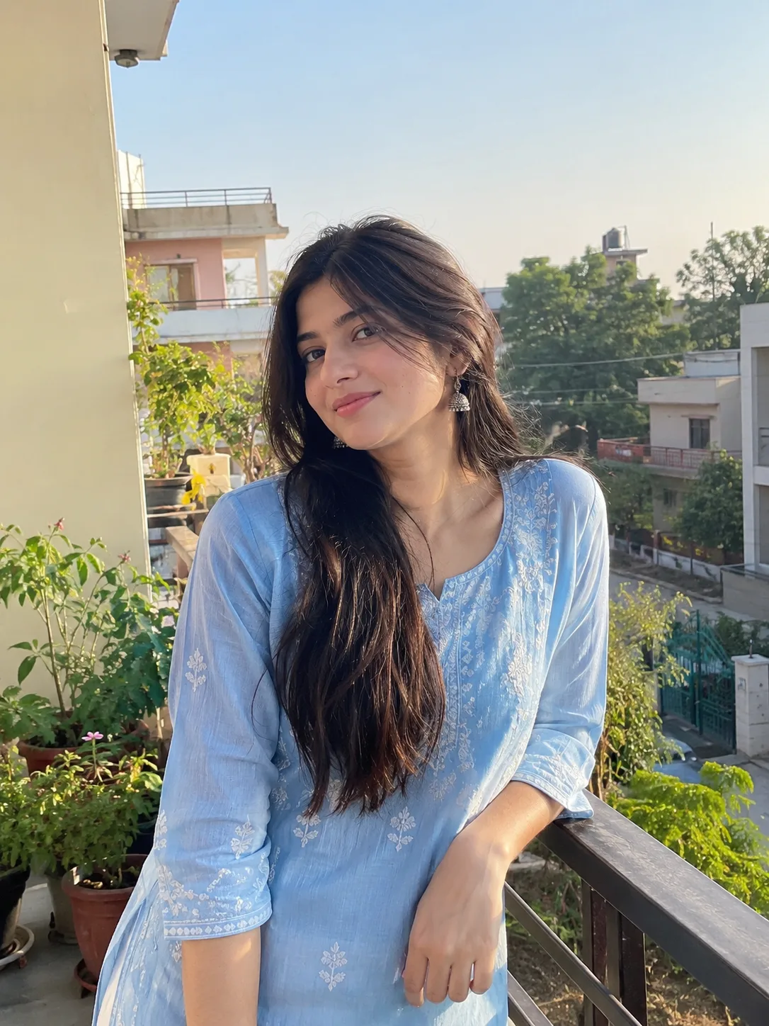 Ultra realistic photograph of a young woman standing on a residential balcony during soft morning light, shot on a real DSLR camera.
