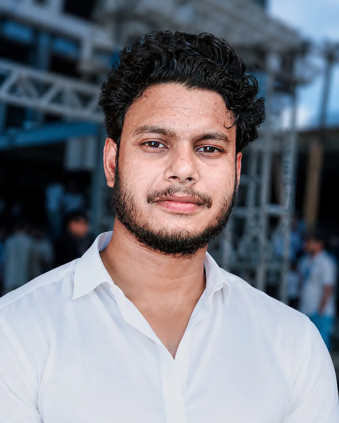 A realistic portrait of a young South Asian man in his mid-20s, looking directly at the camera with a calm, slightly confident expression.