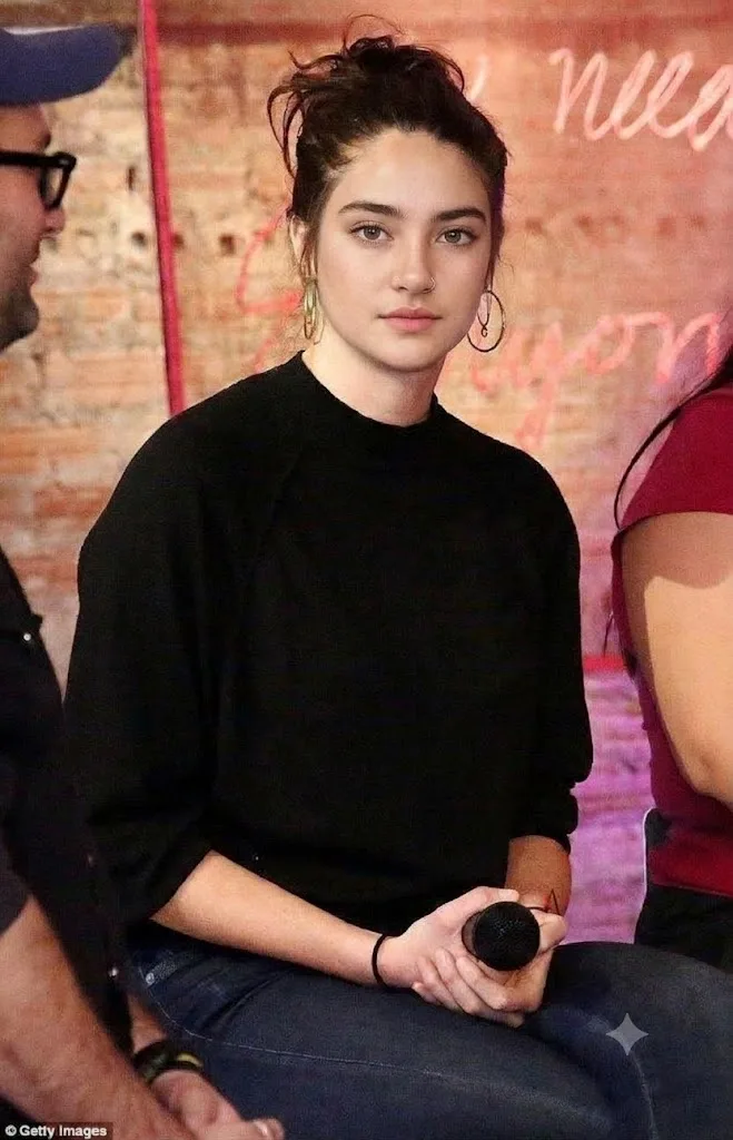 A candid, high-detail photograph of a young woman sitting indoors during a panel discussion.