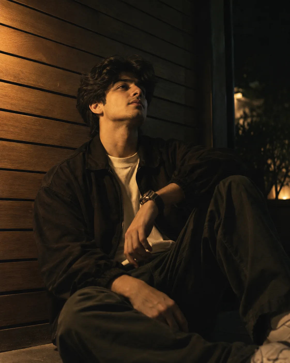 Photorealistic cinematic Half body zoom out portrait of any person sitting casually against a horizontal wooden slat wall, one knee raised,