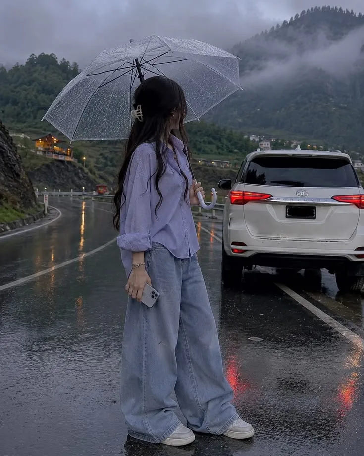 Create an ultra-photorealistic cinematic travel photograph of a fictional young adult woman standing on a wet mountain road during a misty