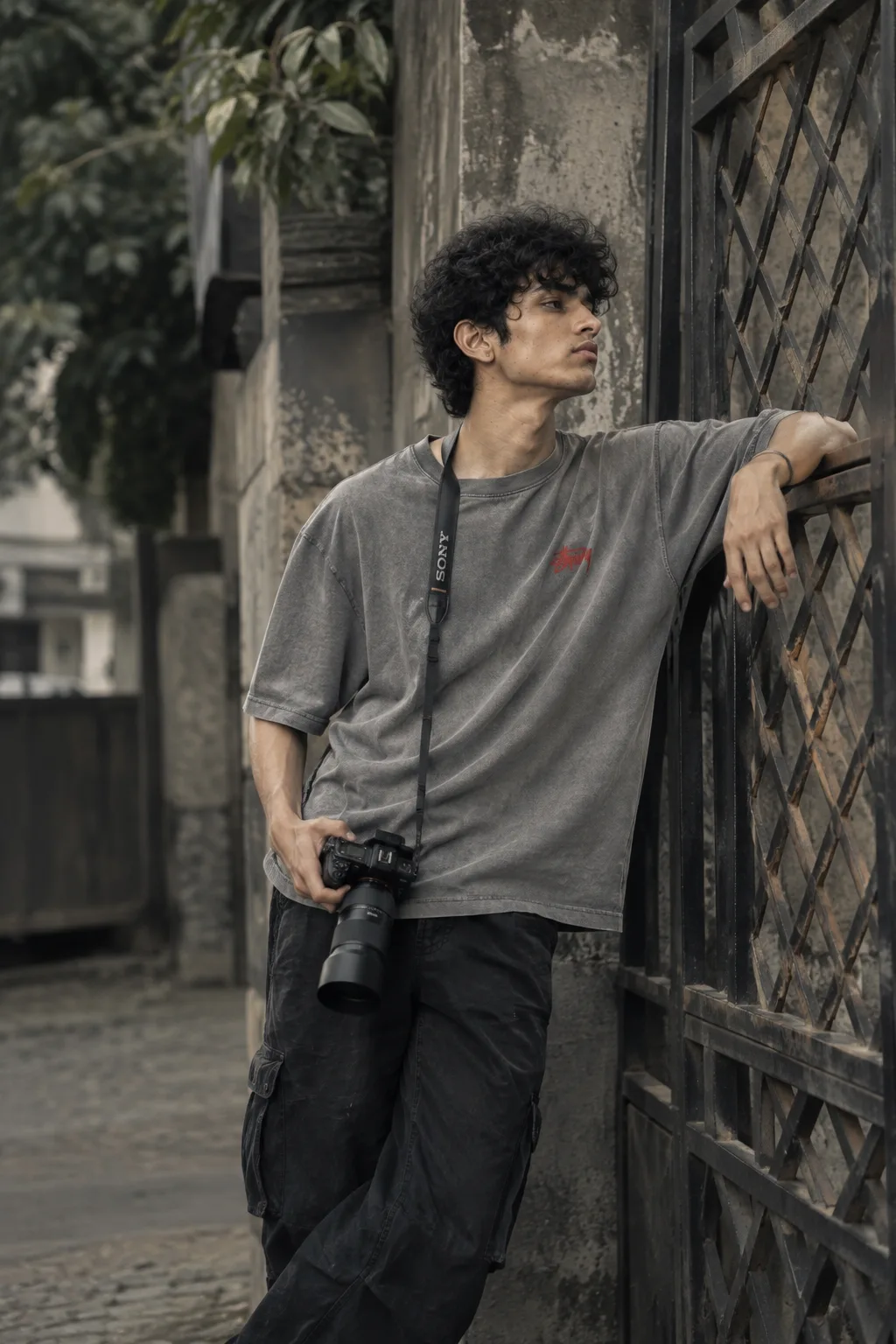 Ultra realistic photograph of a young Indian man standing beside a rustic diamond-lattice iron gate on a quiet old urban street, shot on a