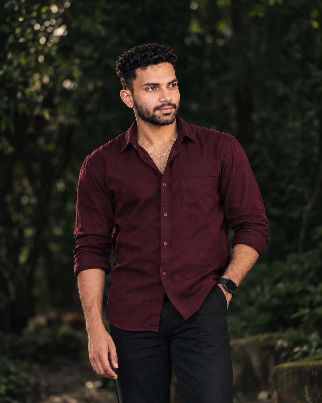 Create a highly realistic cinematic portrait photograph of a young South Asian male standing outdoors in a dark lush green environment.