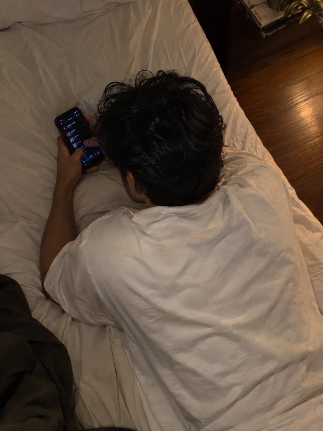 A realistic candid overhead photograph of a young South Indian man lying comfortably on a bed, viewed from directly above and slightly