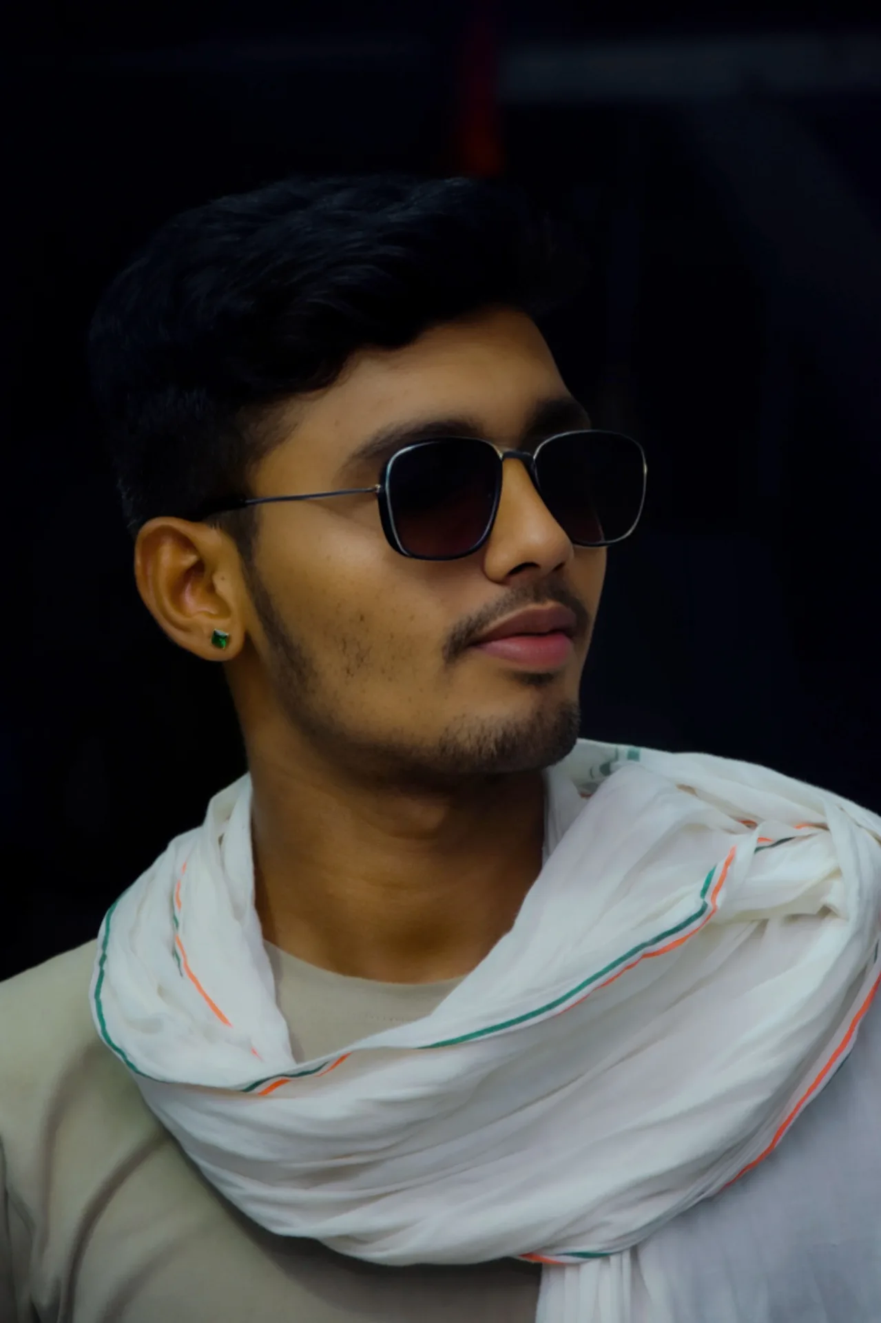 Ultra-realistic cinematic portrait of a young South Asian man, photographed in a dark low-key studio setting.