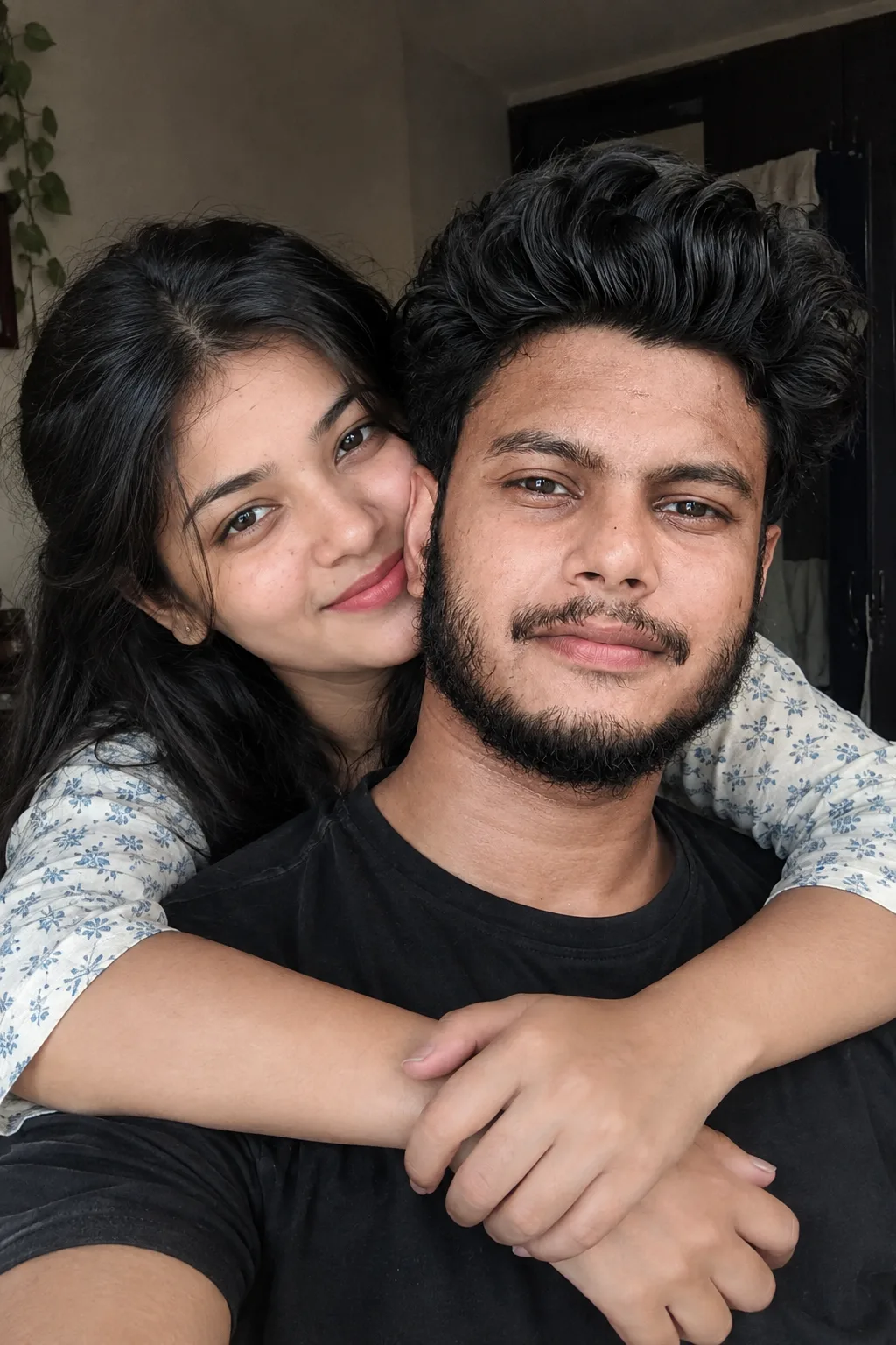 young loving couple cuddling indoors, embraced from behind, gently enveloped around the chest area with both hands.