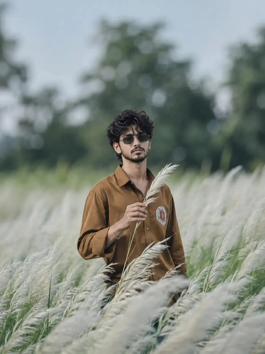 A cinematic realistic portrait of a young man standing in a field of tall white kans grass, wearing a brown full-sleeve shirt and black