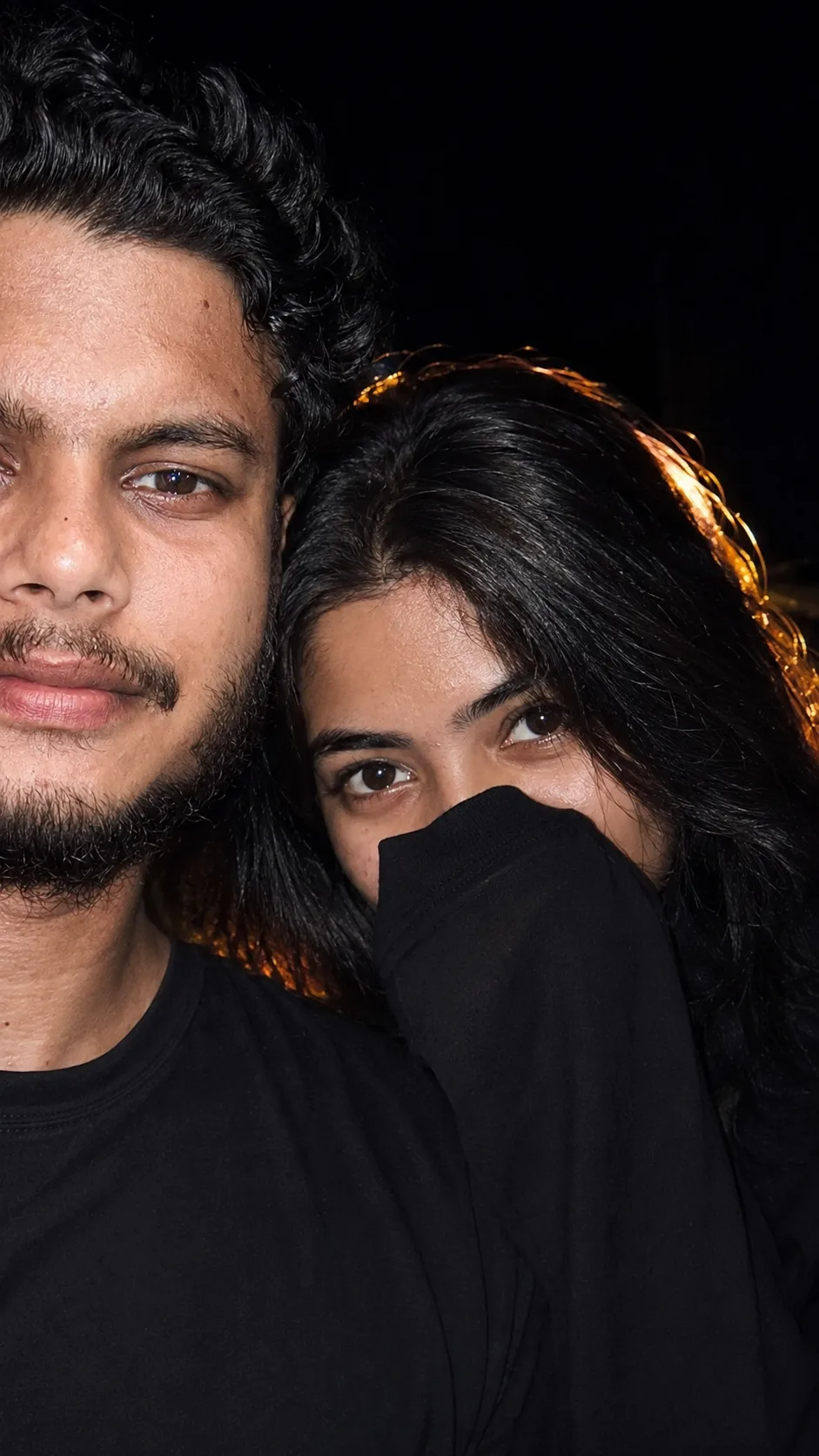 A close-up nighttime portrait of a young South Asian couple.