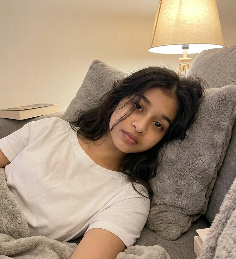 Edit the image so the same woman is lying comfortably on a soft couch, turned slightly on her side with her head resting against a cushion.