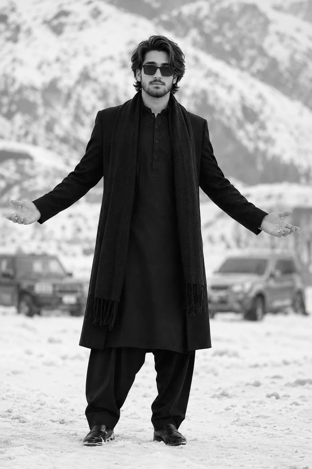 A full-body, ultra-realistic monochrome fashion portrait of a young South Asian man standing confidently in the center of a snowy mountain