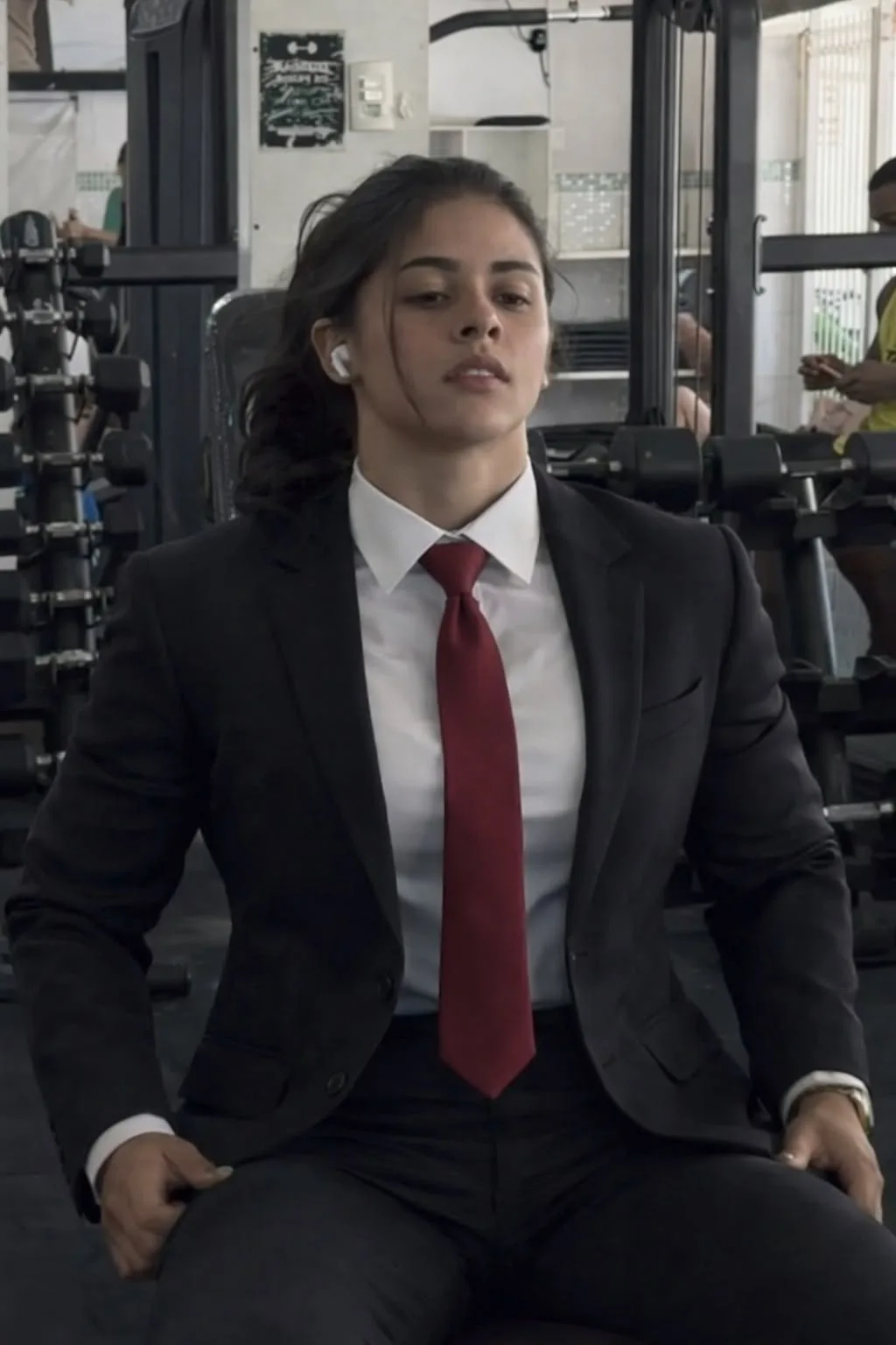 Ultra-realistic cinematic portrait of the same woman from the reference image, seated confidently on a modern gym exercise machine.