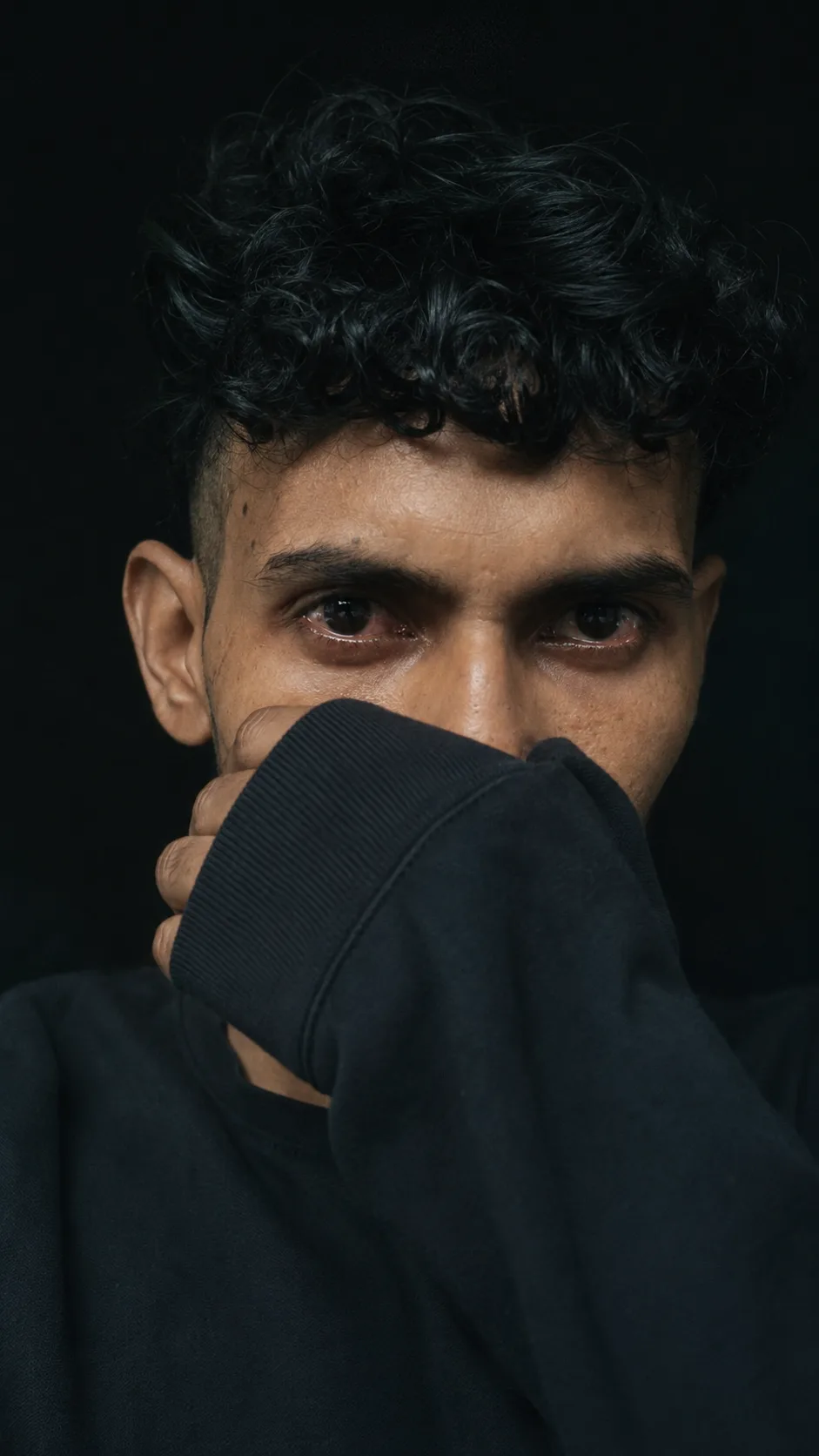 Ultra-realistic, moody close-up portrait of the same young man, preserving his face, hairstyle, skin tone, gold earrings, and features.