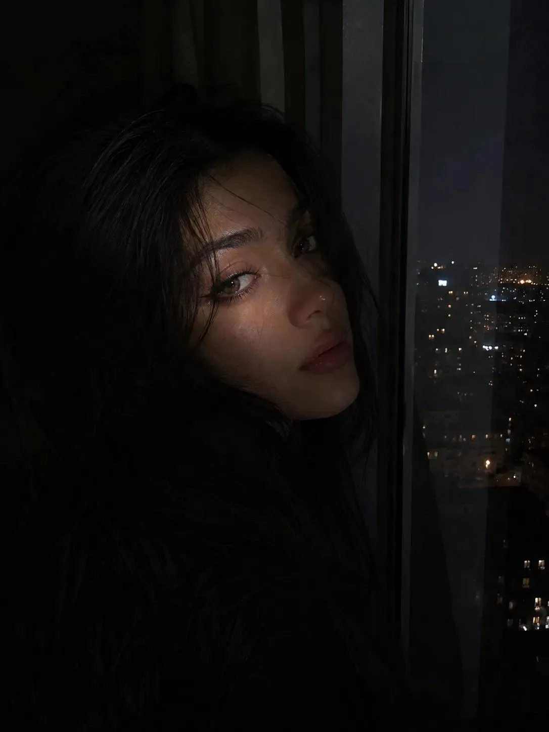 A highly realistic cinematic night portrait of a beautiful young adult South Asian woman standing beside a large bedroom window at night.
