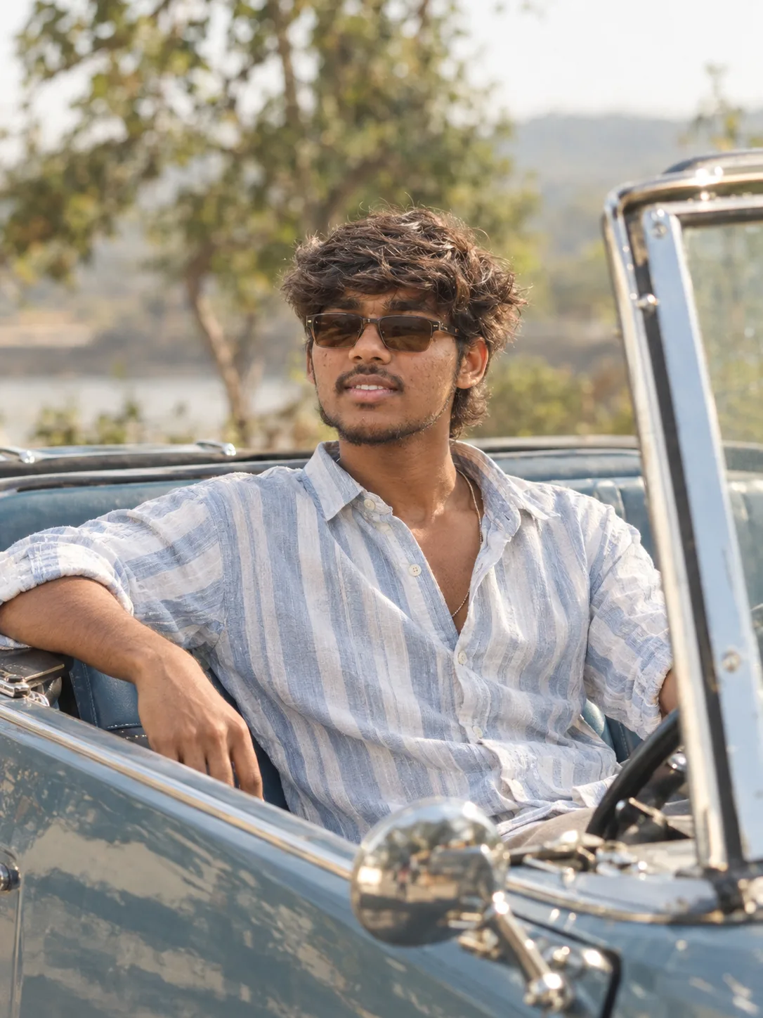 Ultra-realistic cinematic lifestyle portrait of a stylish young South Asian man sitting casually inside a vintage open-top vehicle,