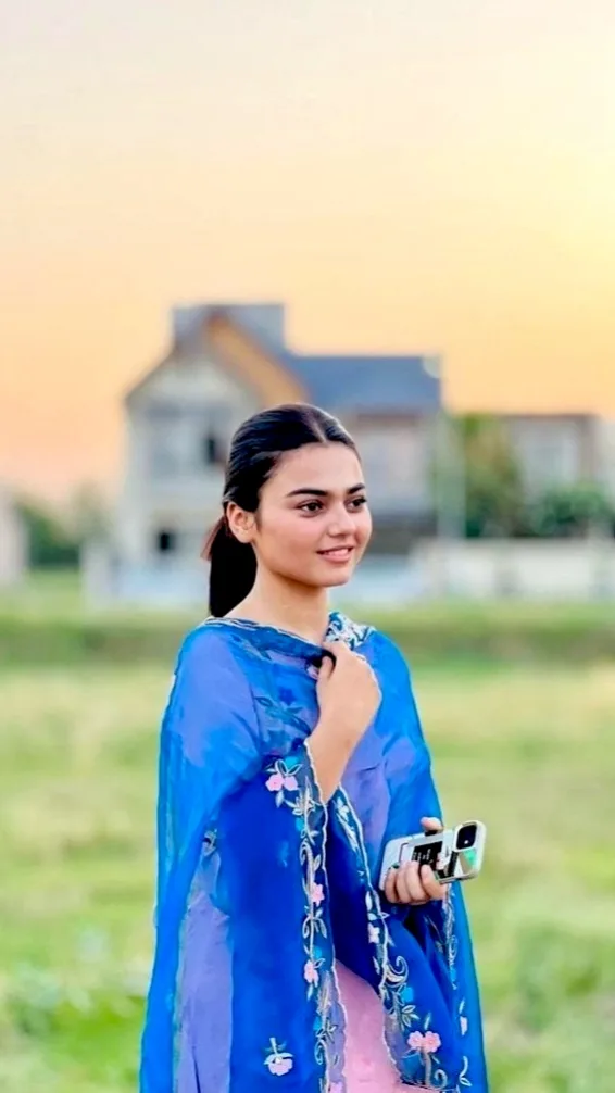 A photorealistic vertical medium shot of the young South Asian woman from the reference image, faithfully preserving her exact recognizable