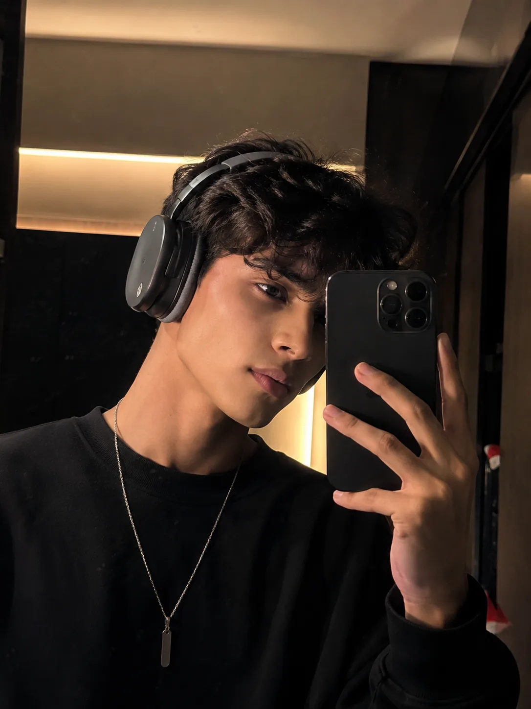 Create a highly realistic close-up mirror selfie of a stylish young boy wearing premium over-ear headphones and an oversized black