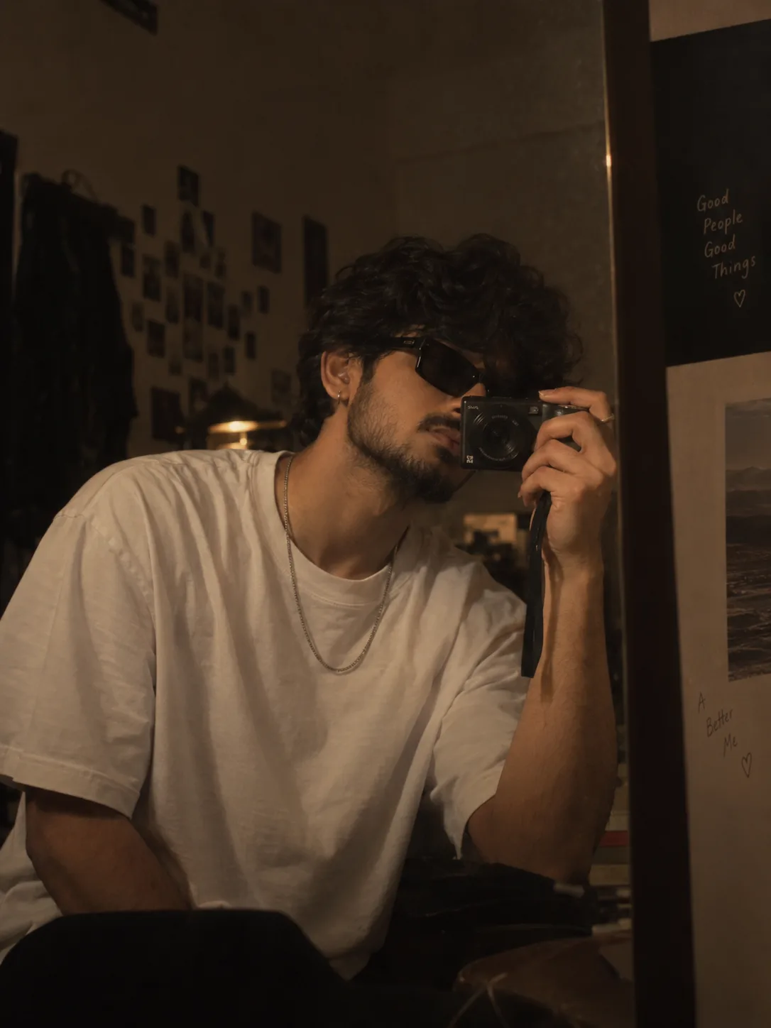A cinematic mirror selfie of a young man with curly black hair, wearing black sunglasses, a nh hite oversized t-shirt, and a thin silver